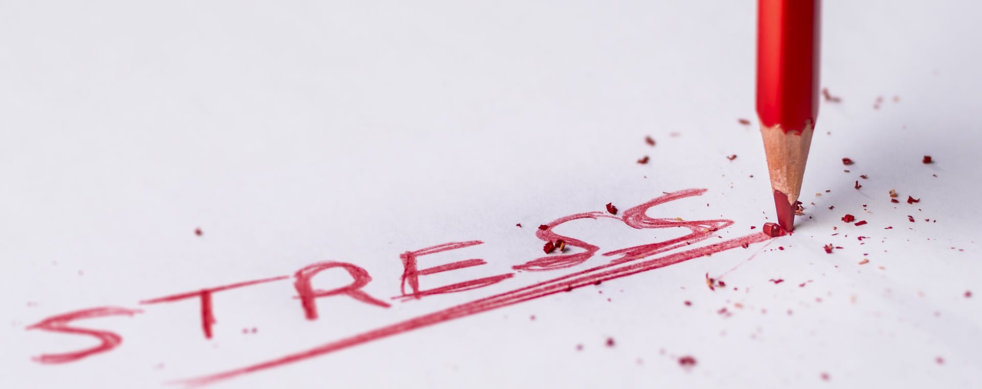 Close-up of a red pencil writing 'stress' on paper, symbolizing pressure and creativity.