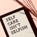 Letter board displaying 'Self Care Isn't Selfish' with artistic shadow on pink background.
