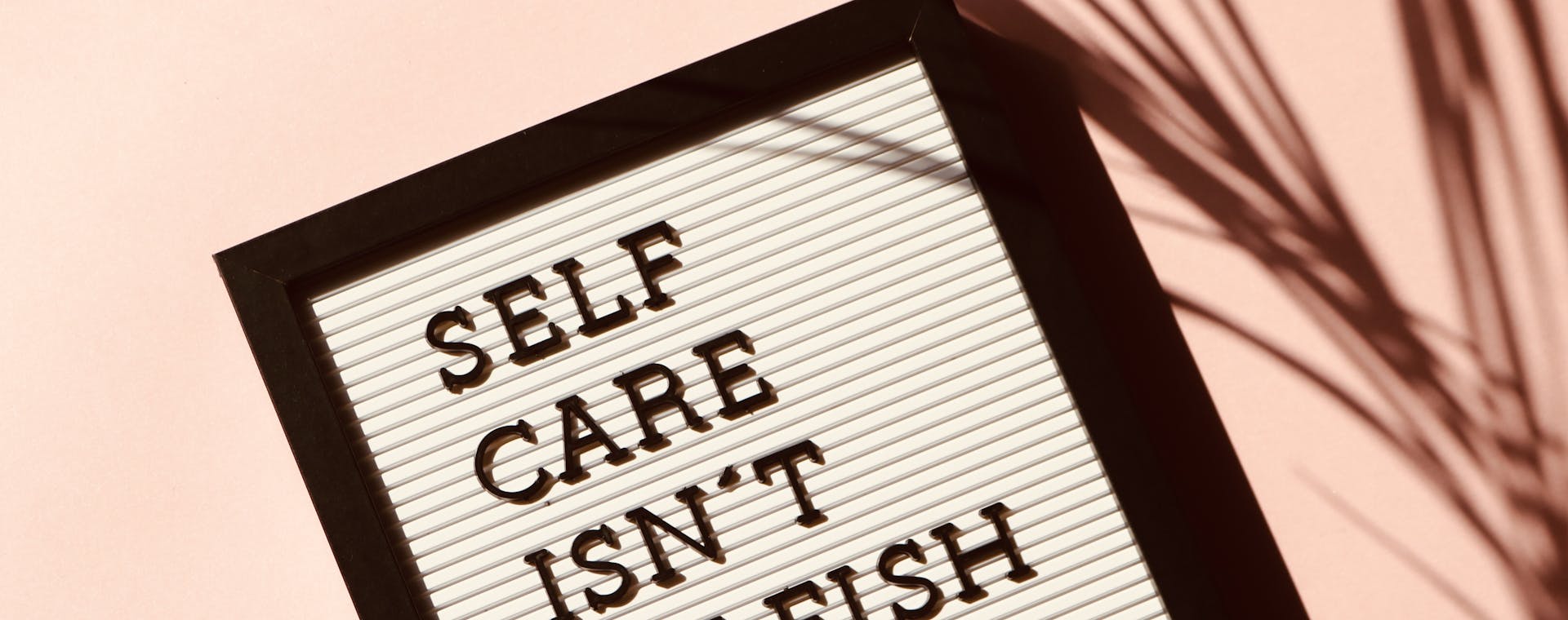 Letter board displaying 'Self Care Isn't Selfish' with artistic shadow on pink background.