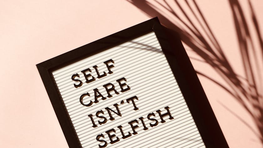 Letter board displaying 'Self Care Isn't Selfish' with artistic shadow on pink background.