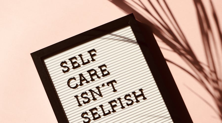 Letter board displaying 'Self Care Isn't Selfish' with artistic shadow on pink background.