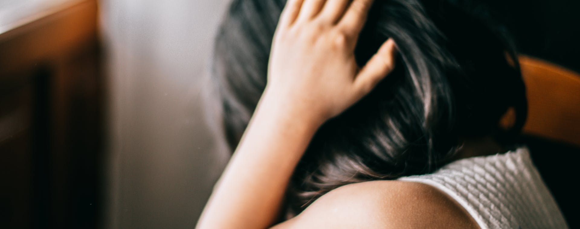 Young girl in emotional distress, sitting indoors with hand on head.