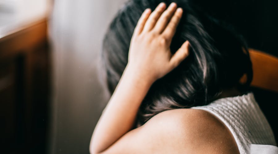 Young girl in emotional distress, sitting indoors with hand on head.