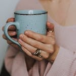 A close-up of a woman's hands holding a blue ceramic mug, wearing a cozy sweater.