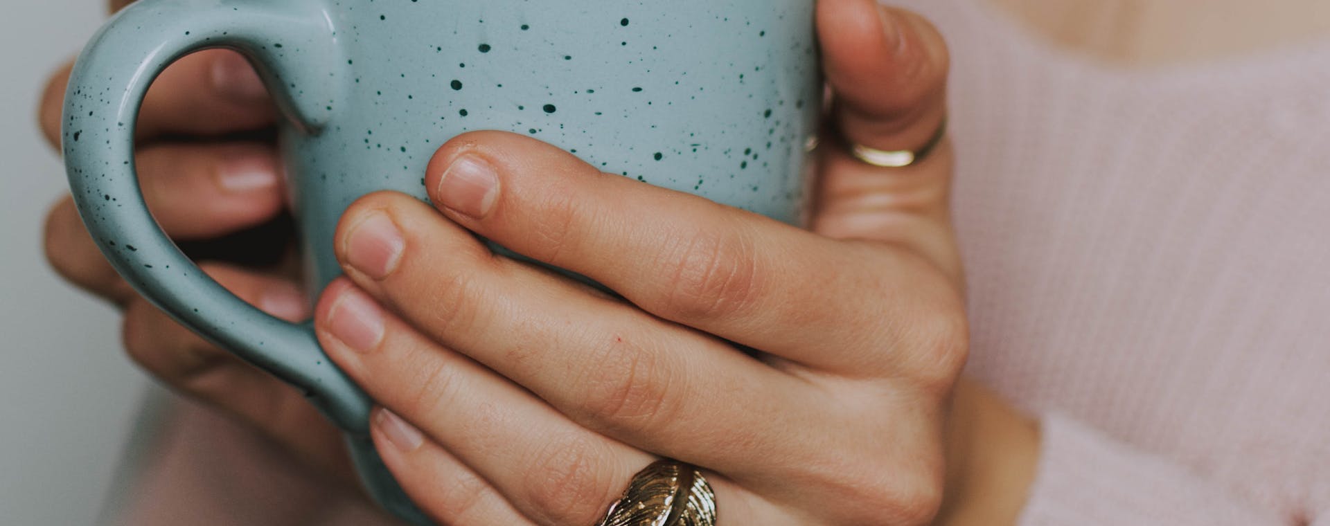 A close-up of a woman's hands holding a blue ceramic mug, wearing a cozy sweater.