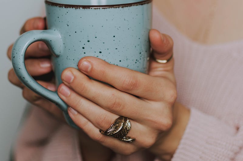 A close-up of a woman's hands holding a blue ceramic mug, wearing a cozy sweater.