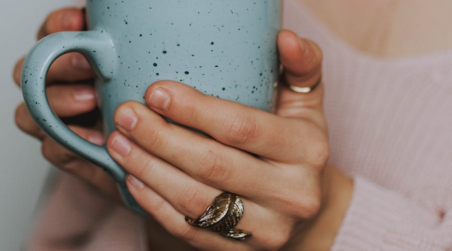 A close-up of a woman's hands holding a blue ceramic mug, wearing a cozy sweater.
