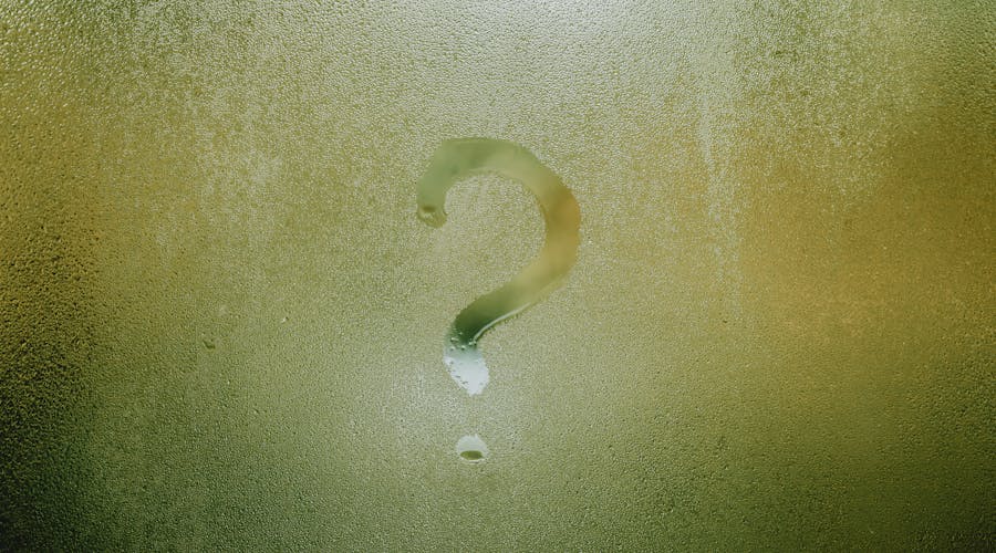 A question mark drawn on foggy glass, evoking curiosity and mystery.