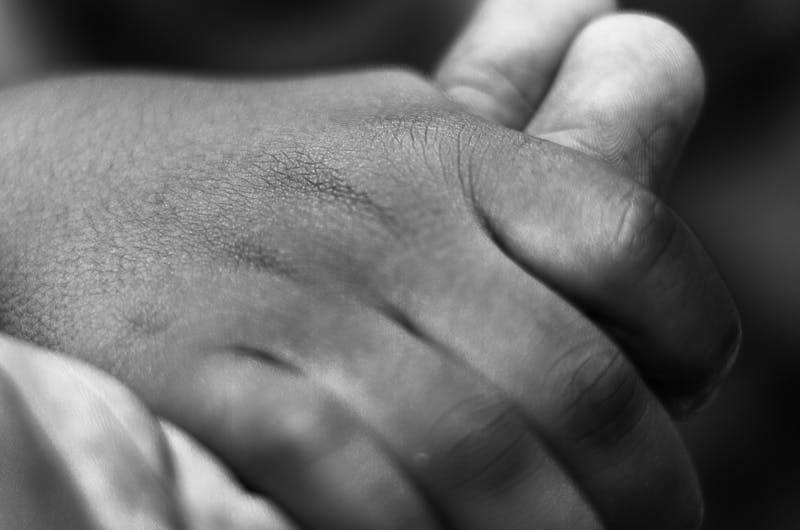 Close-up black and white photo of a child's hand holding an adult's, symbolizing care and connection.